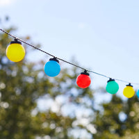 Bunte Outdoor-Lichterkette mit gelben, blauen, roten und grünen Kugelleuchten vor unscharfem Gartenhintergrund