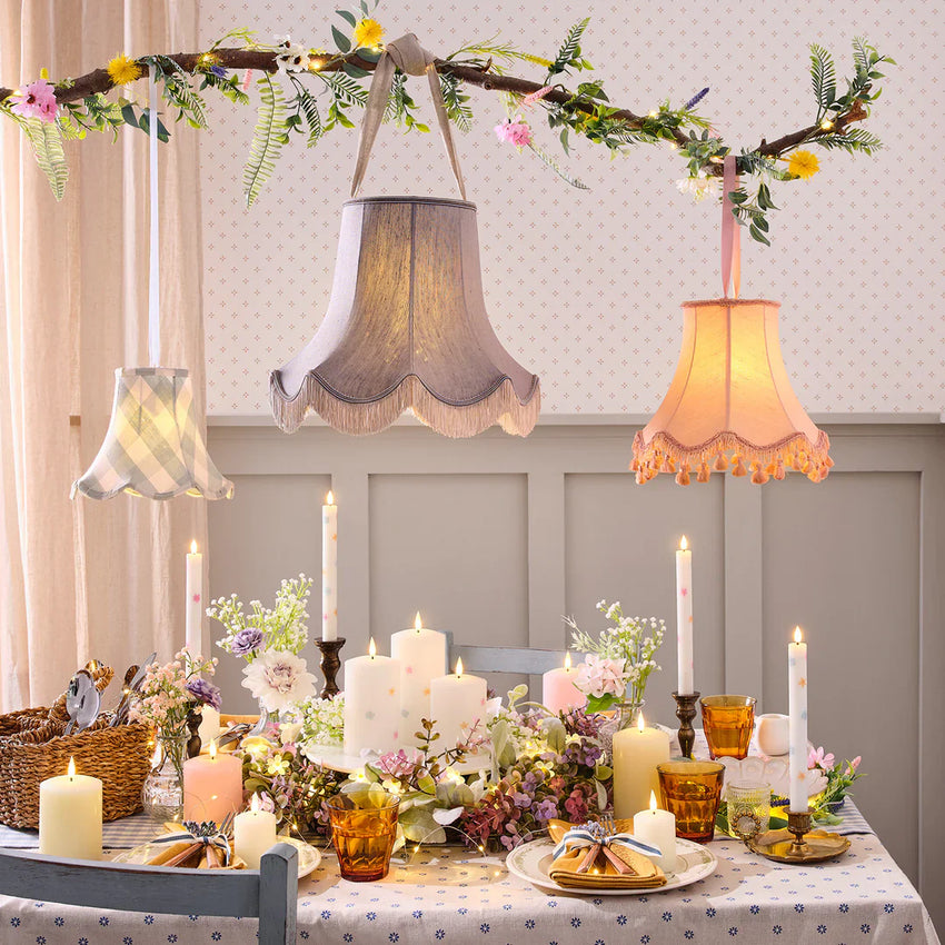 Frühlingshaft gedeckter Ostertisch mit Kerzen, Blumen, Vintage-Lampenschirmen und floraler Hänge-Deko