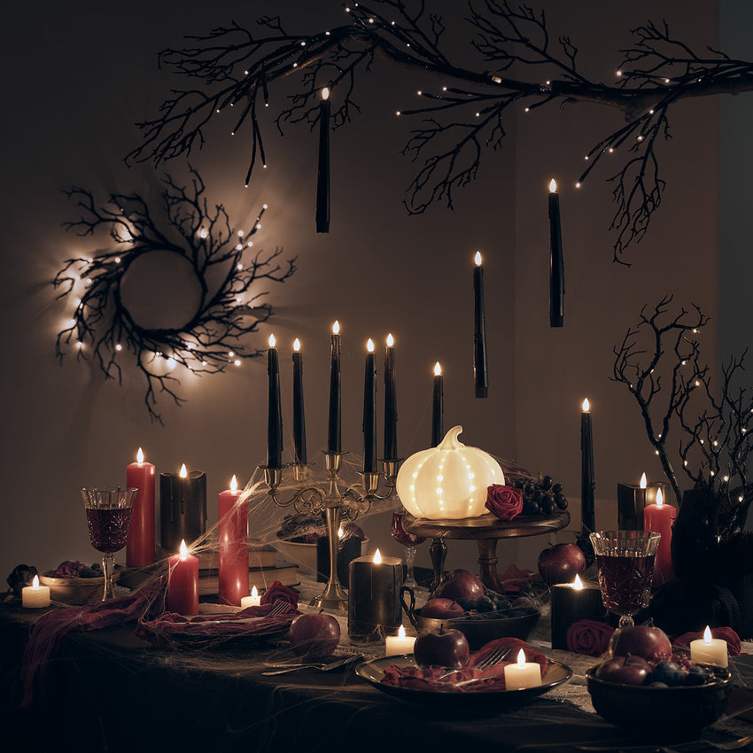Halloween-Partytisch mit Kerzen, leuchtendem Kürbis und dunklen Zweigen als stimmungsvolle Deko.