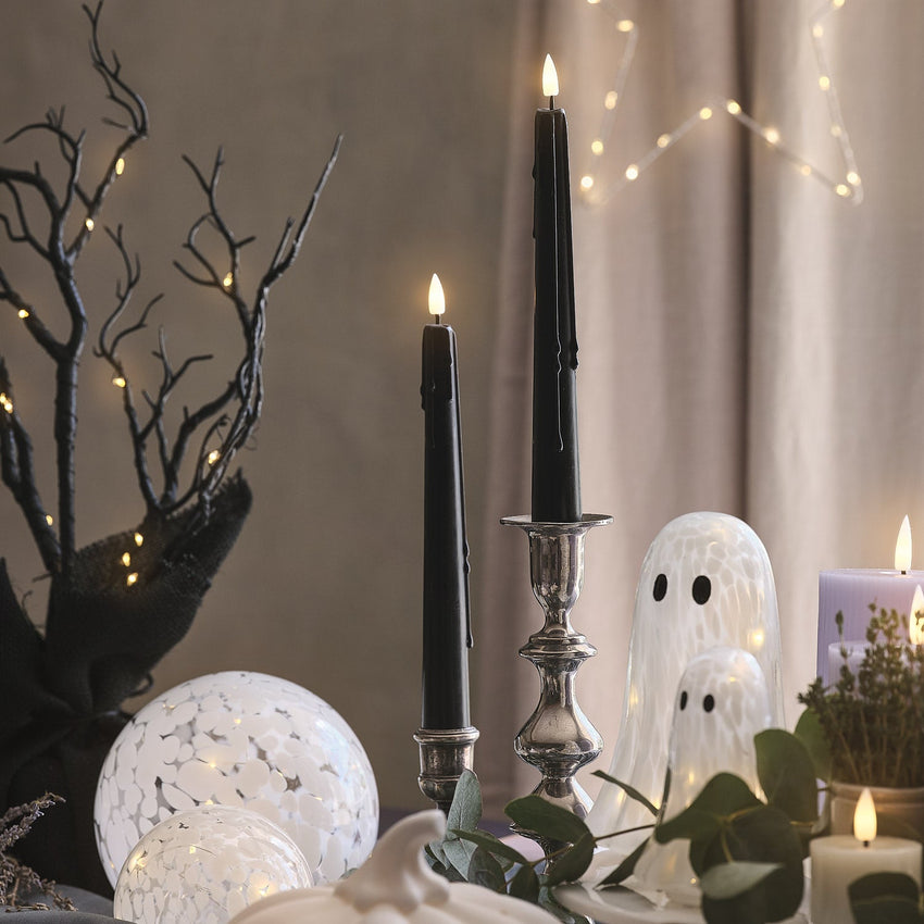 Schwarze LED Kerzen und Halloween-Laterne mit Hexenmotiv auf einer Holzkommode