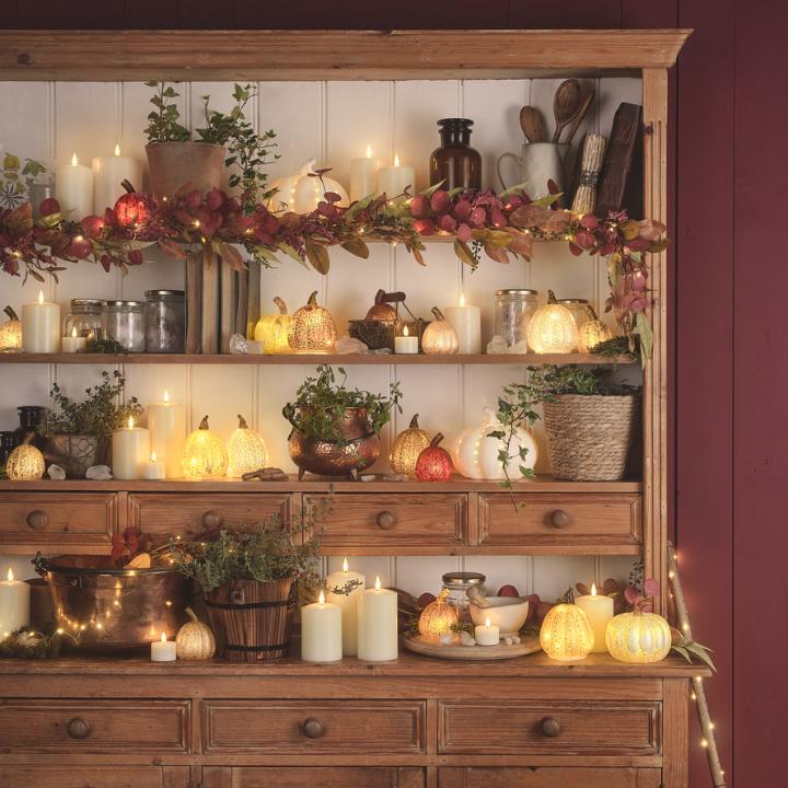 Herbstlich dekorierter Küchenschrank mit leuchtenden Kürbissen, Kerzen, Blättern und Lichterketten.