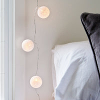 Lichterkette mit weißen Stoffbällen an der Wand neben einem Bett