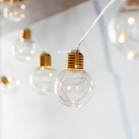 Glühbirnen-Lichterkette mit warmweißen LEDs an weißem Kabel vor hellem Hintergrund.