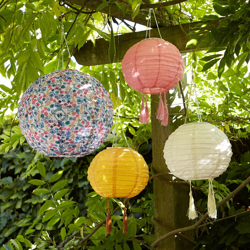 Bunte Lampions in verschiedenen Größen hängen zwischen grünen Blättern im Garten.