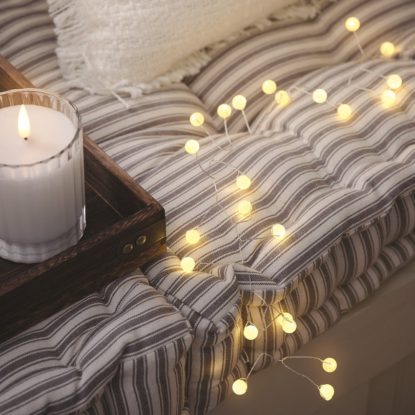 Gemütliche Fensterbank mit warmweißer Lichterkette, Kerze und gestreiftem Kissen.