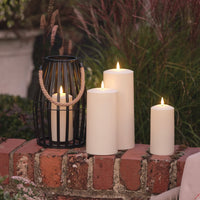 Outdoor-Deko mit LED-Kerzen und schwarzer Laterne auf einer Backsteinmauer im Garten.