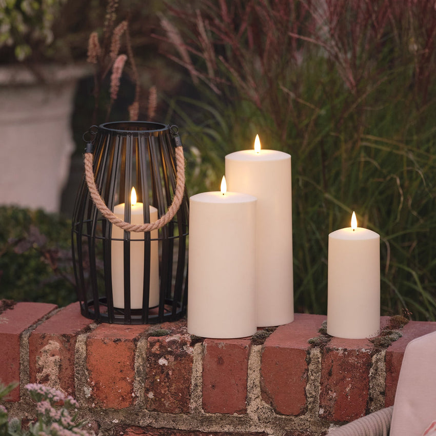 Outdoor-Deko mit LED-Kerzen und schwarzer Laterne auf einer Backsteinmauer im Garten.