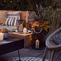 Sommerlich dekorierte Outdoor-Lounge mit Kerzen, Laternen, Kissen und warmen Lichtern.