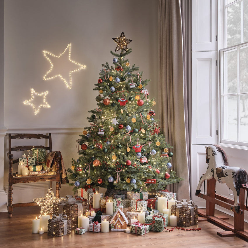 Geschenke und Lichterkette mit Holzsternen auf einem Sessel, davor ein Dekozweig mit Eicheln und Tannenzapfen
