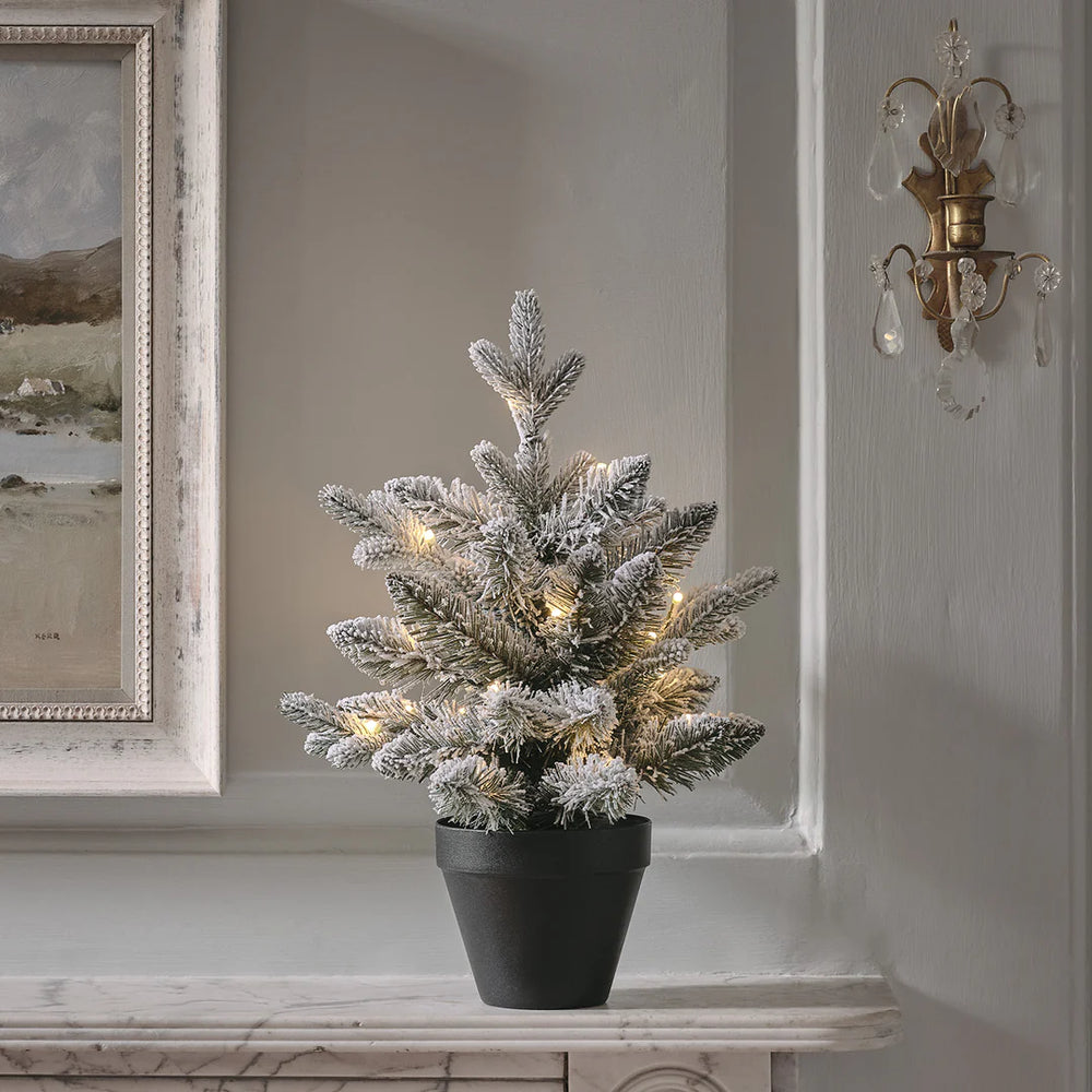 45 cm hoher verschneiter LED-Weihnachtsbaum im schwarzen Topf auf Kaminsims vor grauer Wand