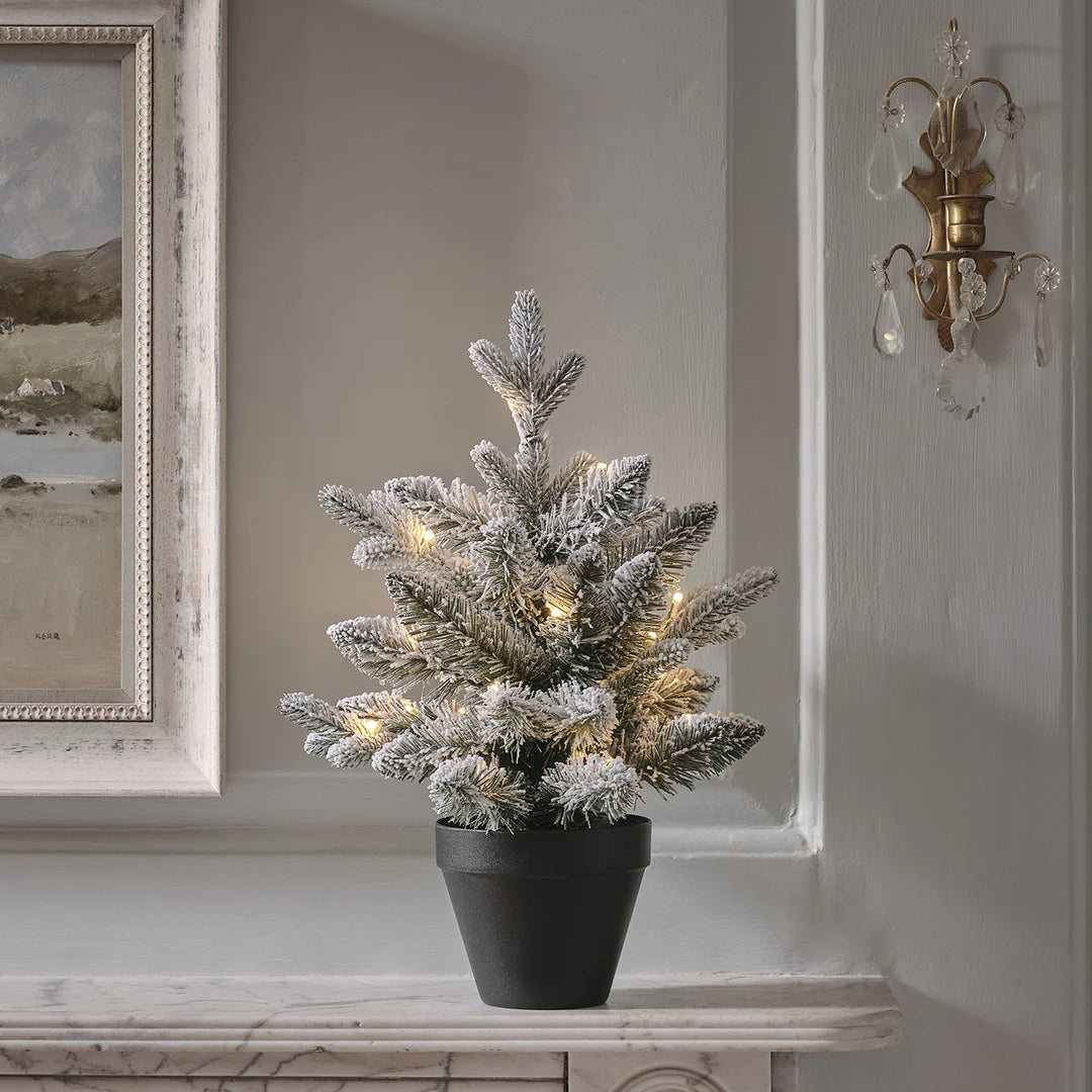 45 cm hoher verschneiter LED-Weihnachtsbaum im schwarzen Topf auf Kaminsims vor grauer Wand