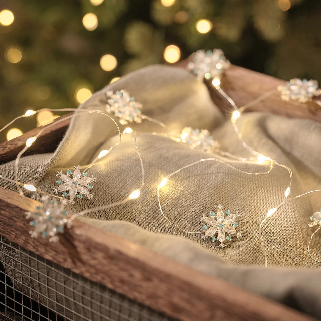 Kristall-Schneeflocken-LED-Lichterkette mit funkelnden Edelstein-Anhängern auf beigefarbenem Stoff, warmweiße LED-Lichter mit bokeh Hintergrund.