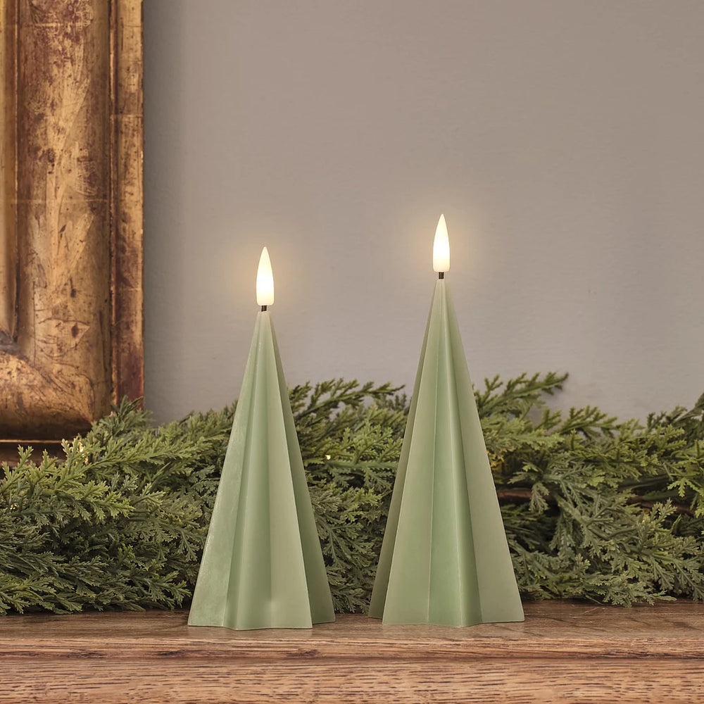 Zwei grüne LED-Spitzkerzen mit realistischen weißen Flammen auf Holztisch, Weihnachtsgrün-Arrangement mit rustikalem goldenem Rahmen im Hintergrund.