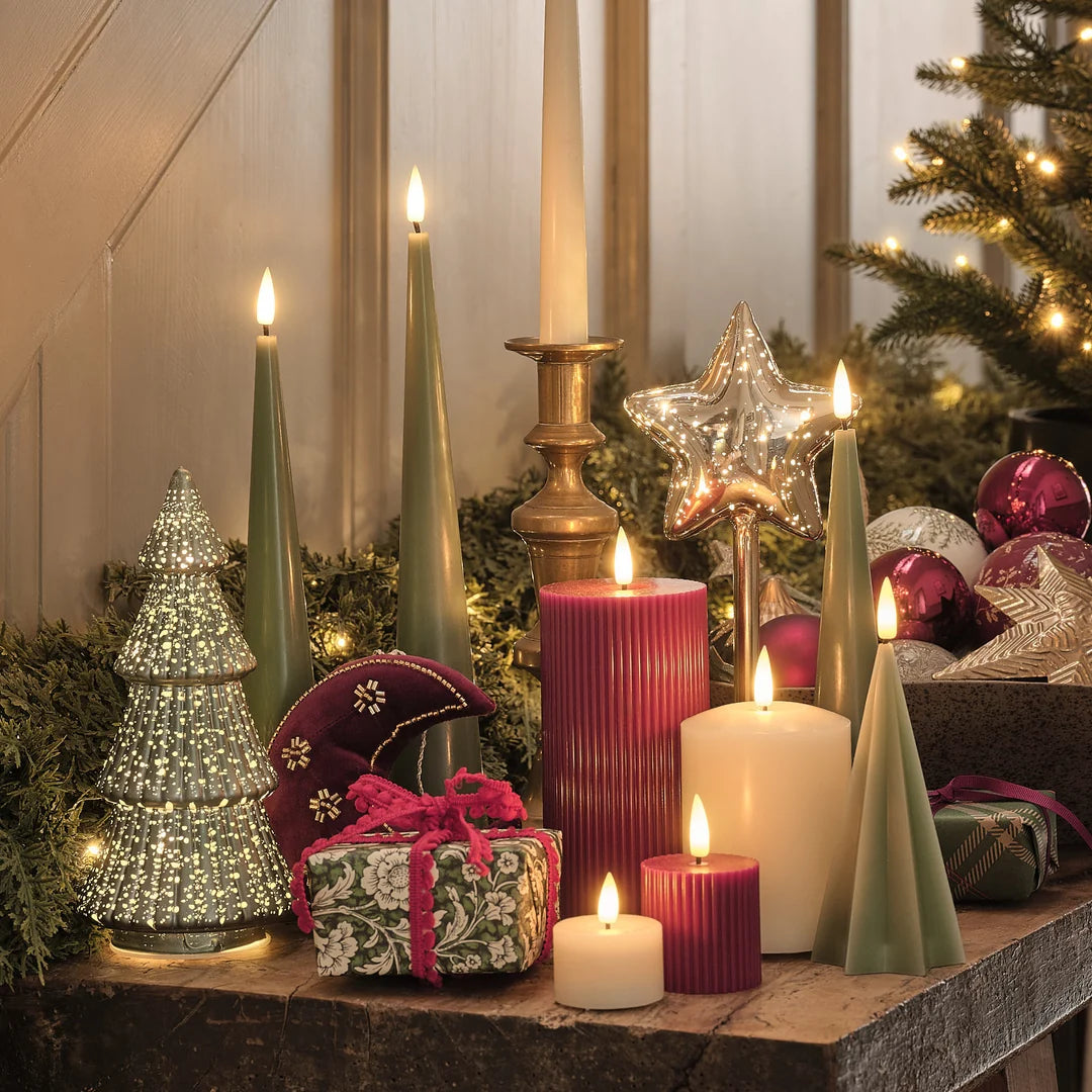 Luxuriöse Weihnachtsdekoration mit grünen LED-Spitzkerzen, cremefarbene und bordeauxrote Kerzen, Kristall-Stern mit LED-Lichtern, Messingkerzenleuchter, Weihnachtskugeln in Bordeaux und Creme, Geschenkbox mit Samtband, Weihnachtsbaum mit warmweißen Lichtern, elegante festliche Tafelgestaltung.