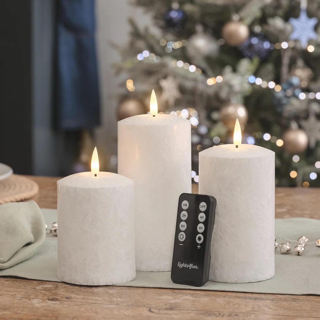 Drei weiße LED-Kerzen mit LED-Flammen, schwarze Fernbedienung mit ON/OFF und Timer-Funktionen (2H, 4H, 6H, 8H) auf Holztisch.