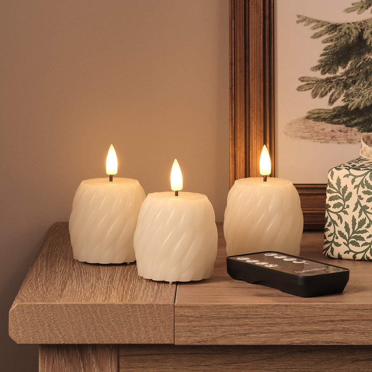 Drei weiße LED-Kerzen mit Fernbedienung in wellenförmiger Textur und warmweißen LED-Flammen auf Holztisch, beige Leinenserviette, verschwommener Tannendekorations im Hintergrund.