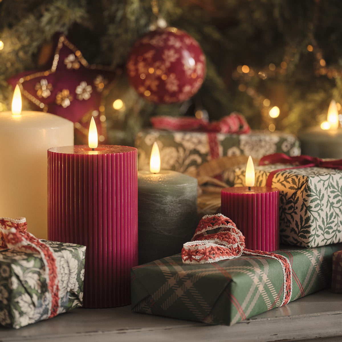 LED-Kerzen in pflaumenfarben mit Weihnachtsgeschenken und Dekoration im Hintergrund