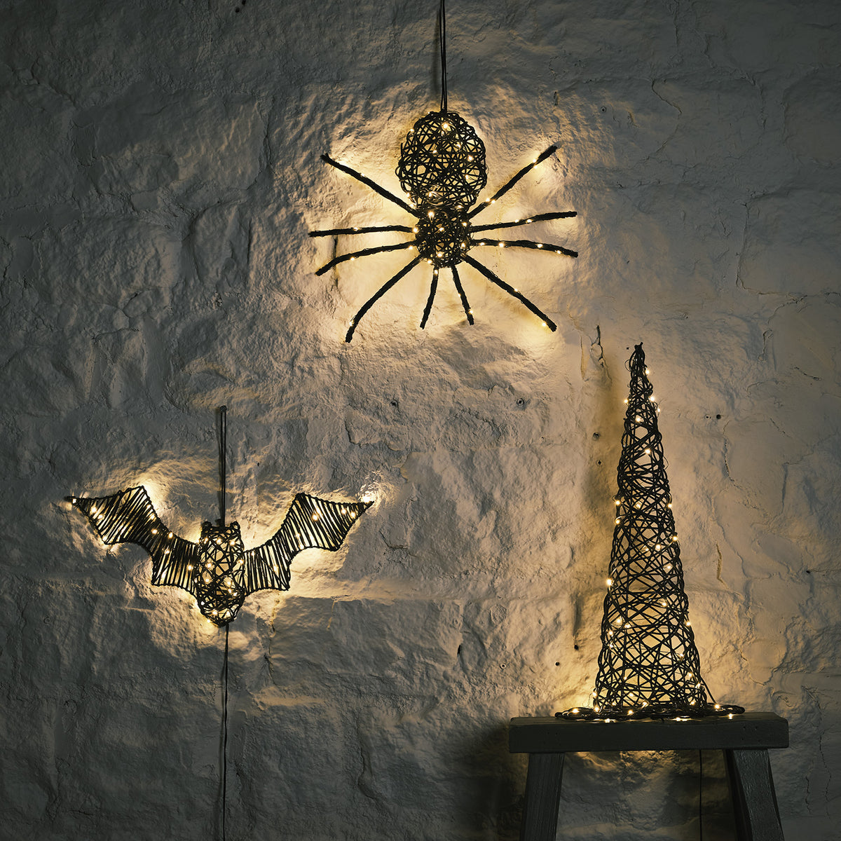 LED beleuchtete Rattan-Spinne, Fledermaus und Hexenhut an weißer Wand im Dunkeln