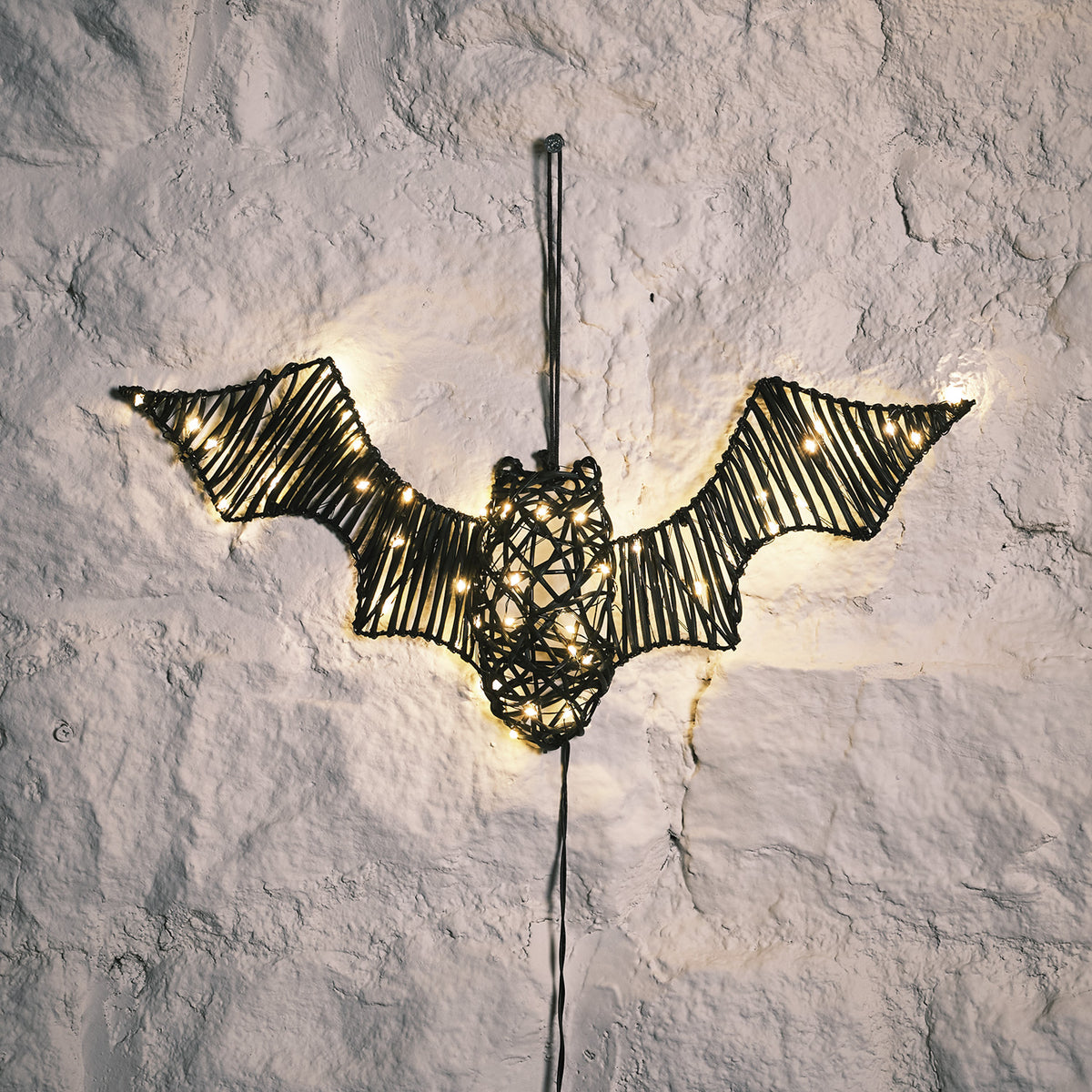 LED beleuchtete Rattan-Fledermaus mit warmweißen Lichtern an weißer Wand