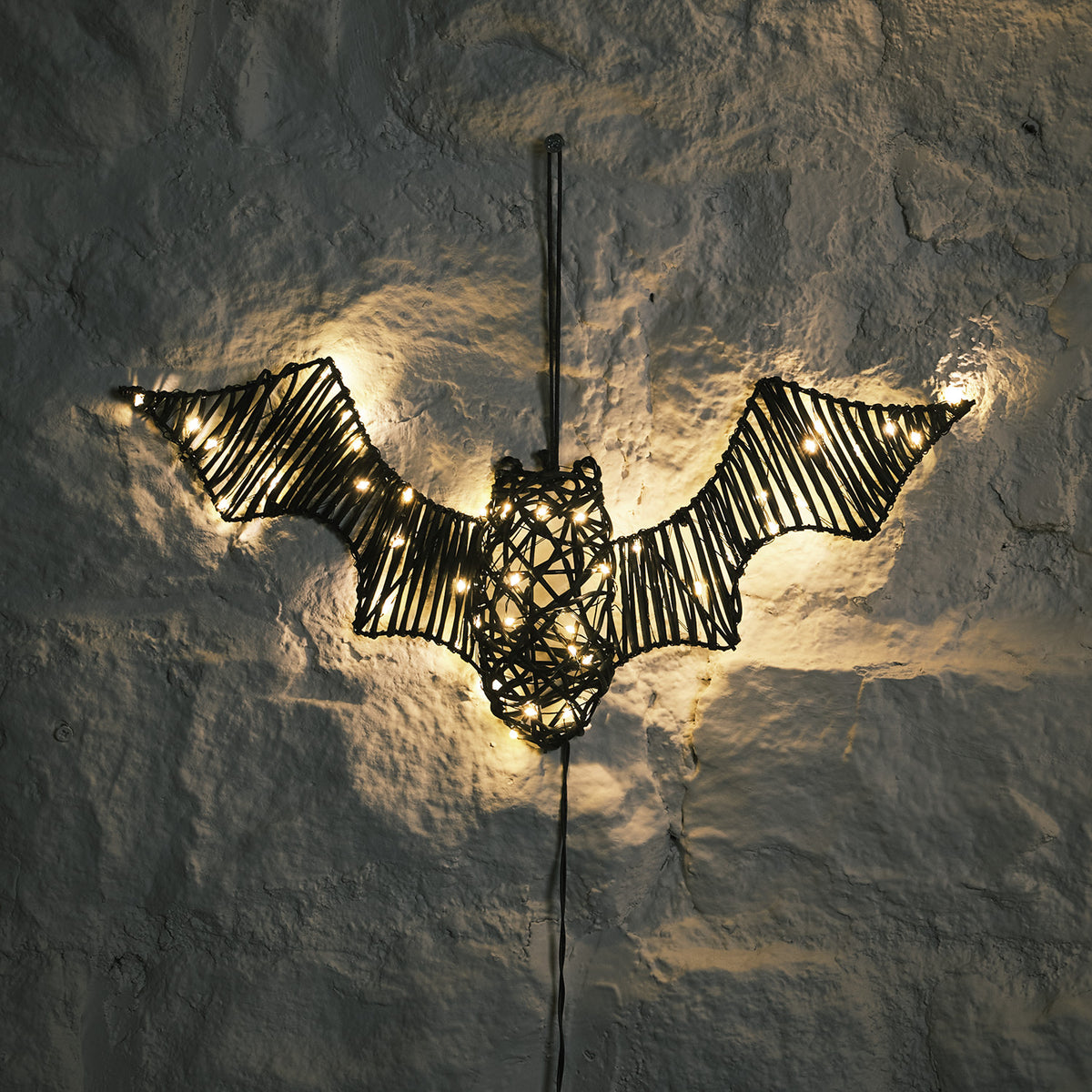 LED beleuchtete Rattan-Fledermaus mit warmweißen Lichtern an weißer Wand