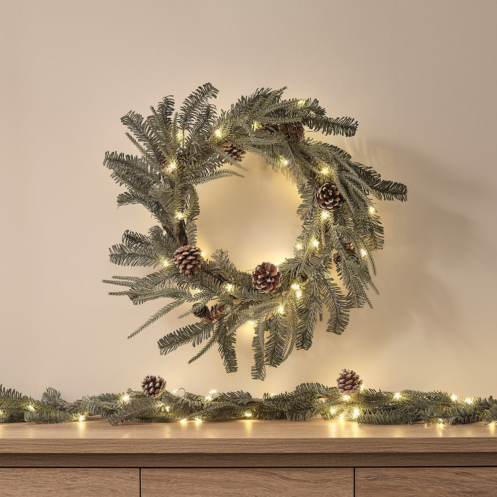 Beleuchteter Weihnachtskranz aus Kunstgrün mit Zapfen an heller Wand