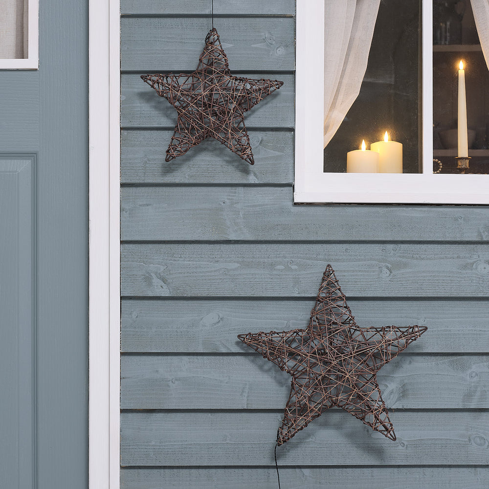 Unbeleuchtete braune Rattan-LED-Sterne in 30 und 40 cm an grauer Holzfassade
