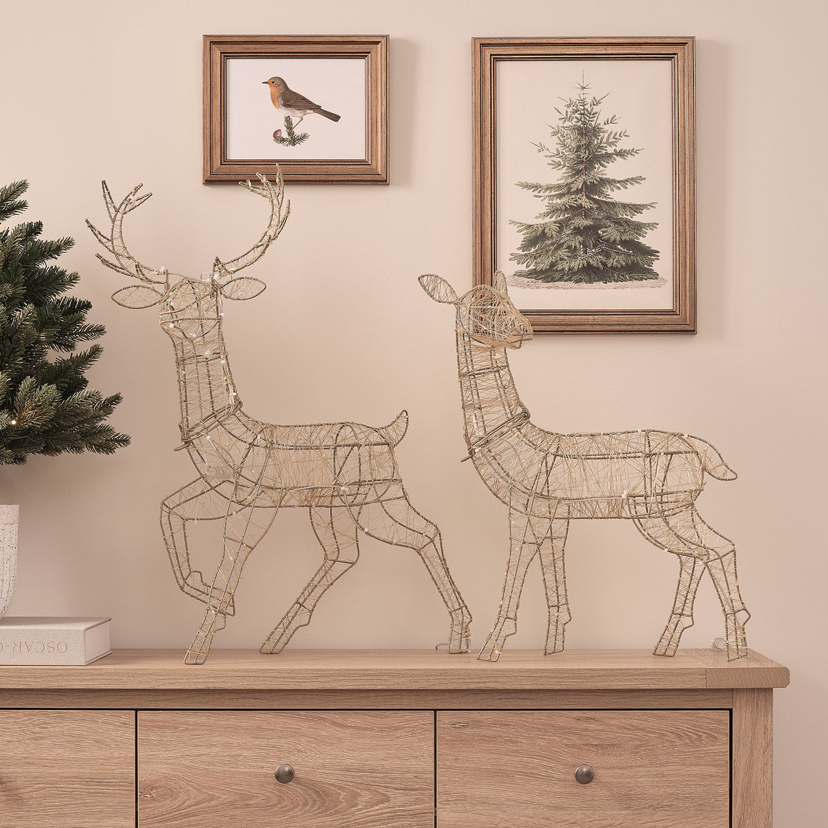 Goldene LED-Rentier-Hirschkuh mit warmweißen Lichtern auf Sideboard vor Wand mit Bildern