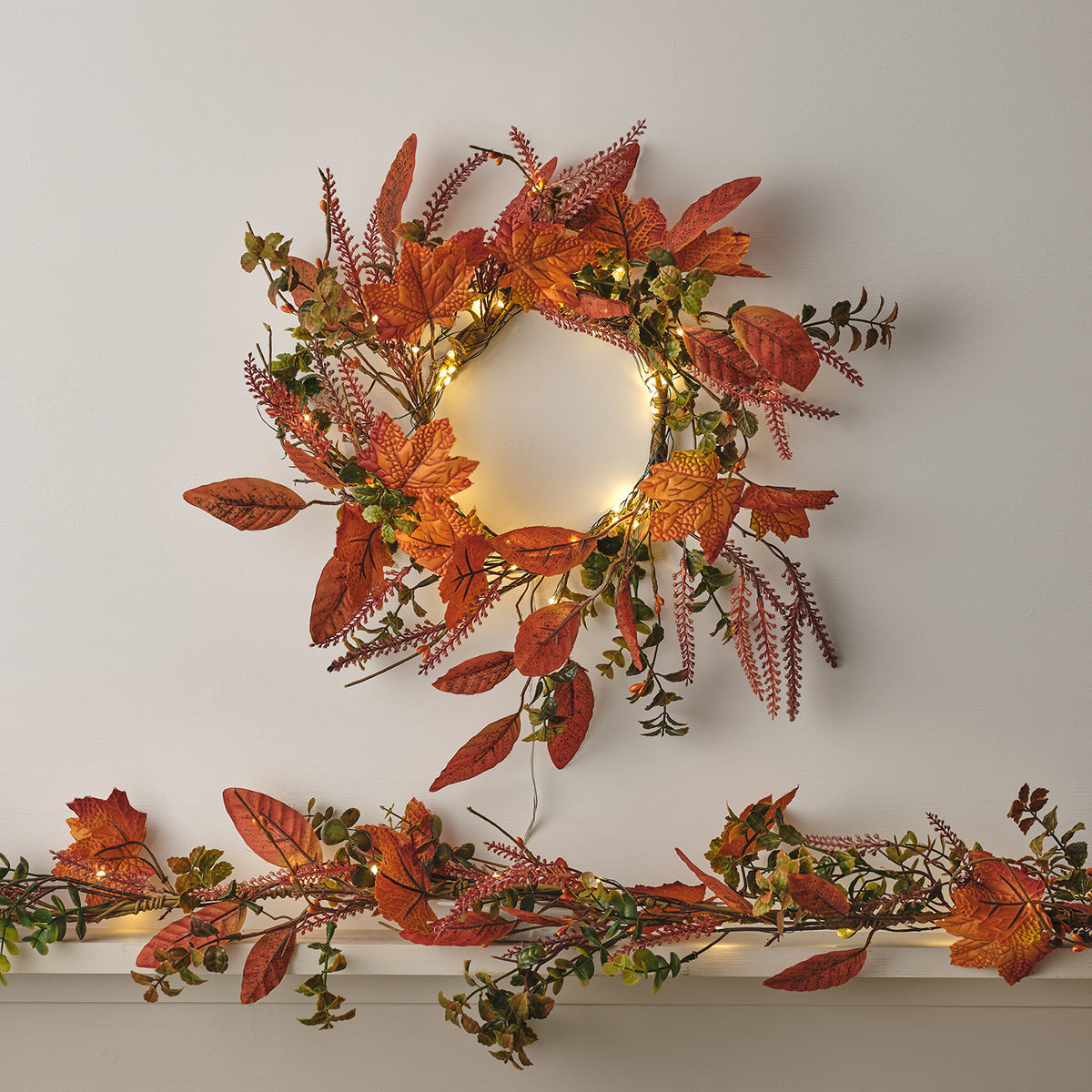 Herbstkranz mit LED-Lichterkette an Wand und passende herbstliche Girlande auf Kaminsims