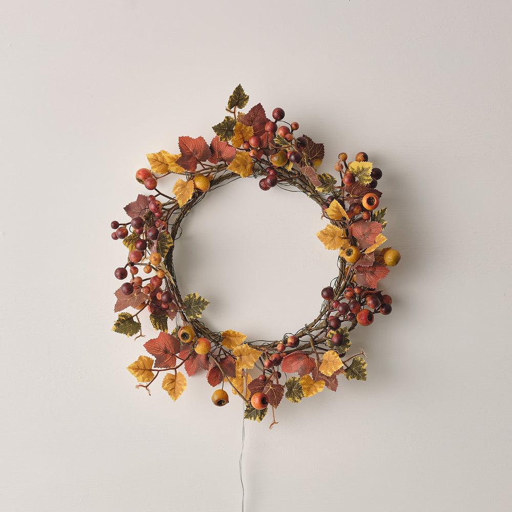 Herbstkranz mit roten und gelben Blättern und Beeren ohne eingeschaltete Lichterkette an weißer Wand