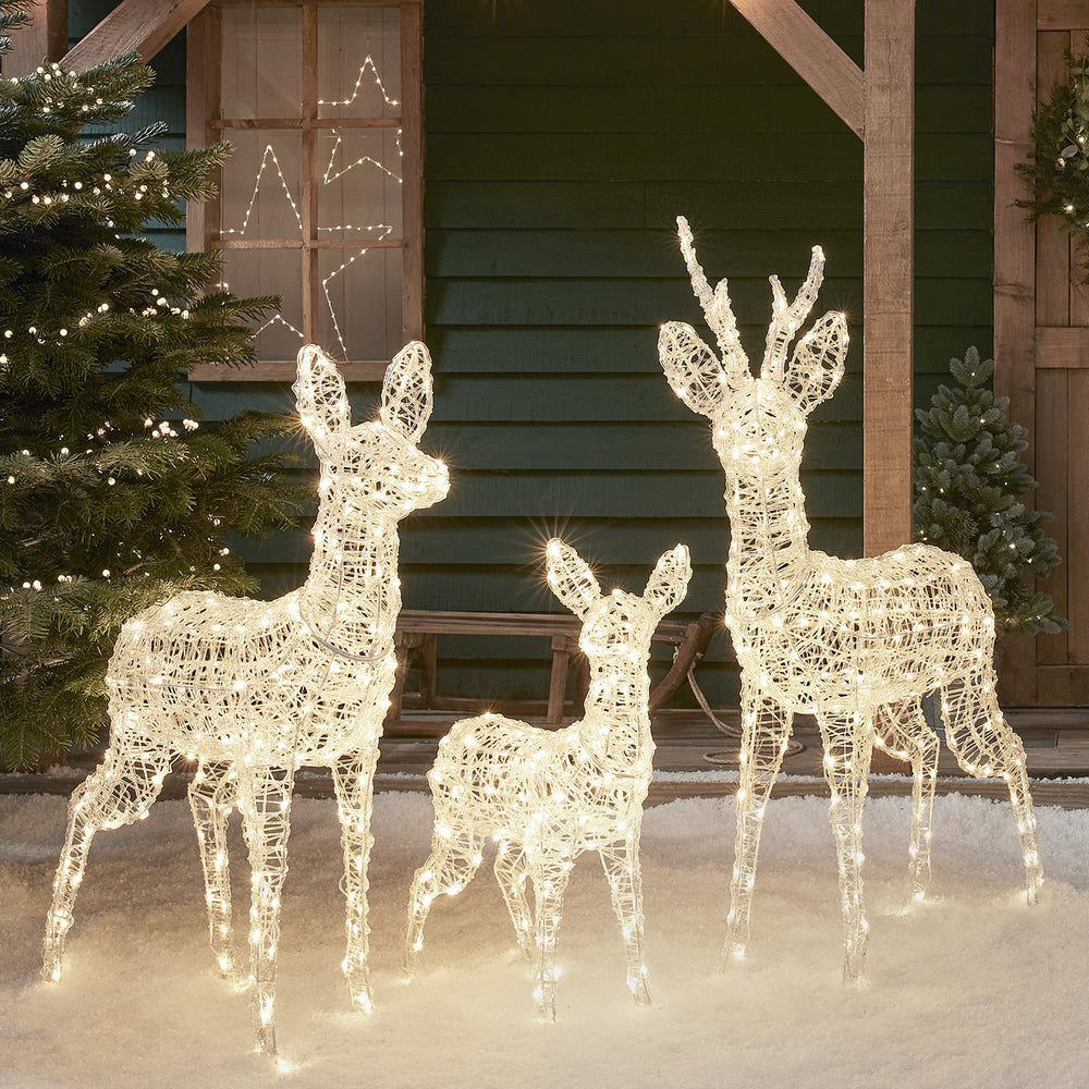 Drei beleuchtete Rentierfiguren aus Acryl mit warmweißen LEDs vor grünem Holzhaus