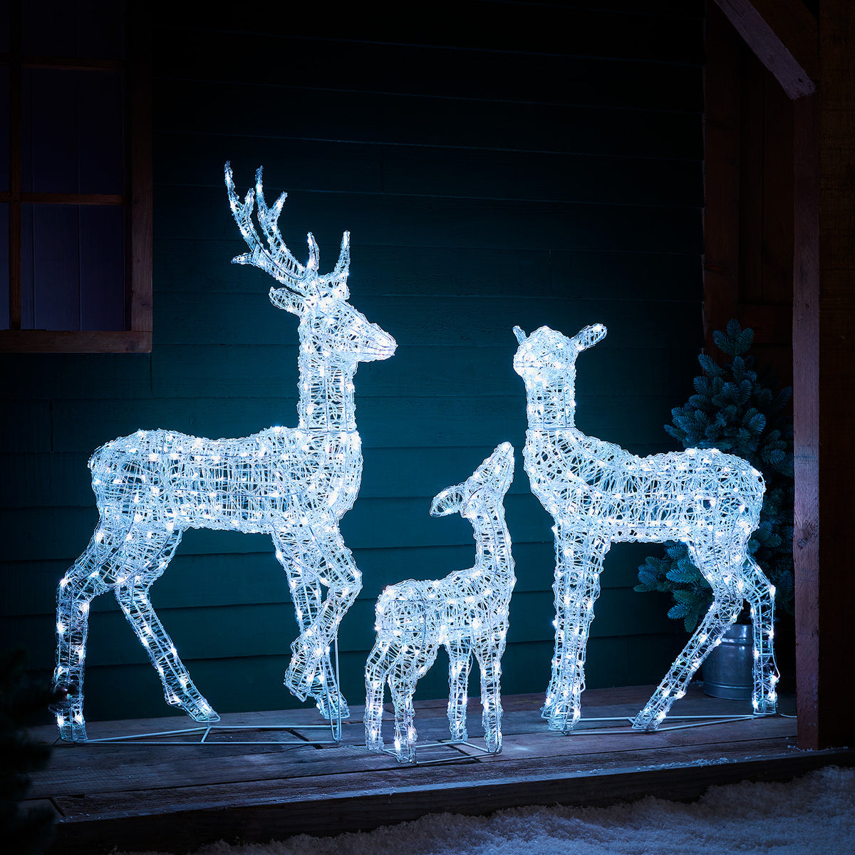 LED-Rentierfamilie weiß leuchtend vor dunkler Holzfassade auf Holzterrasse