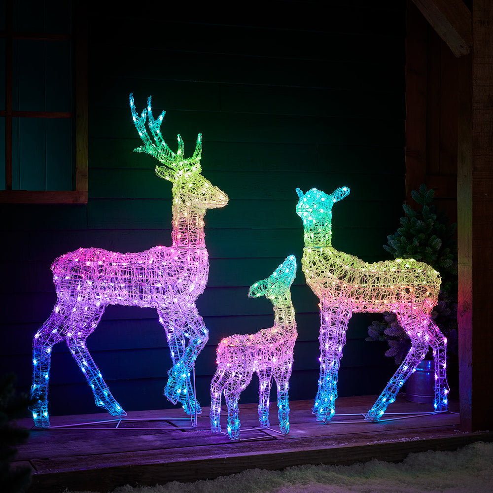 LED-Rentierfamilie bunt leuchtend vor dunkler Holzfassade auf Holzterrasse