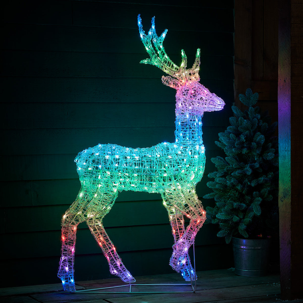LED-Hirsch bunt leuchtend vor dunkler Holzfassade auf Holzterrasse