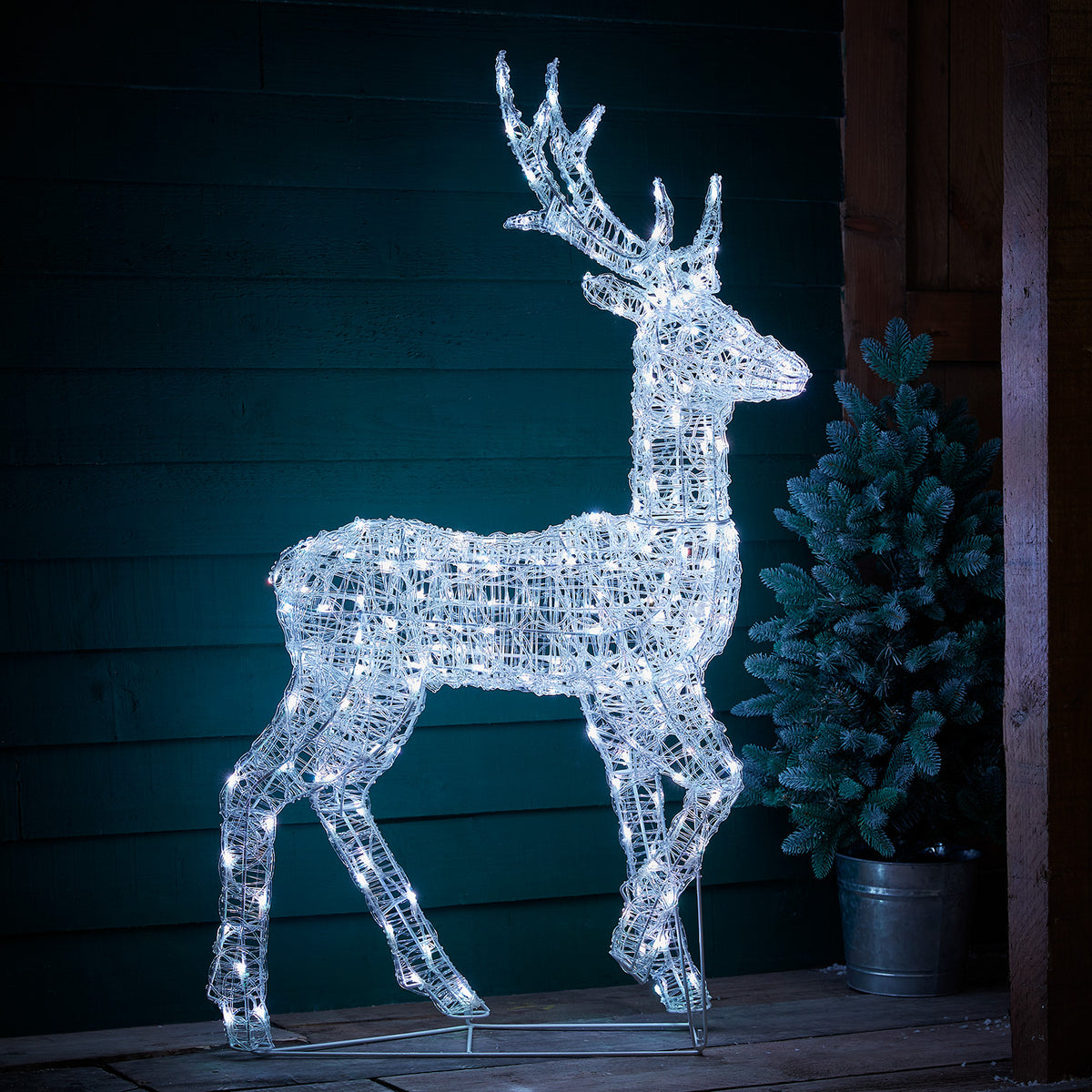 LED-Hirsch pink leuchtend vor dunkler Holzfassade auf Holzterrasse