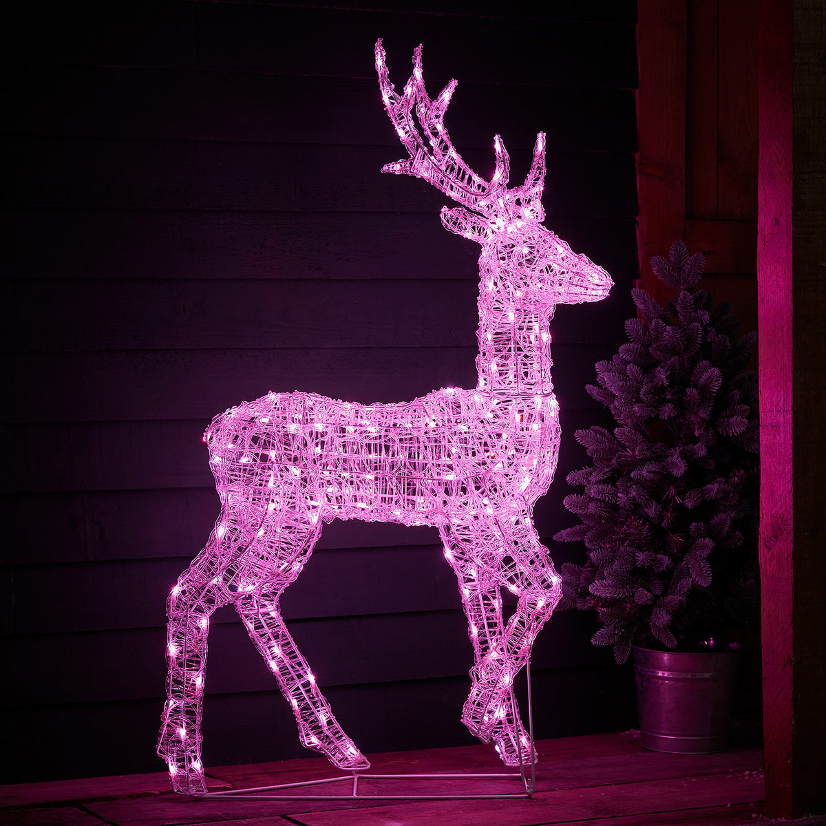 LED-Hirsch grün und blau leuchtend vor dunkler Holzfassade auf Holzterrasse
