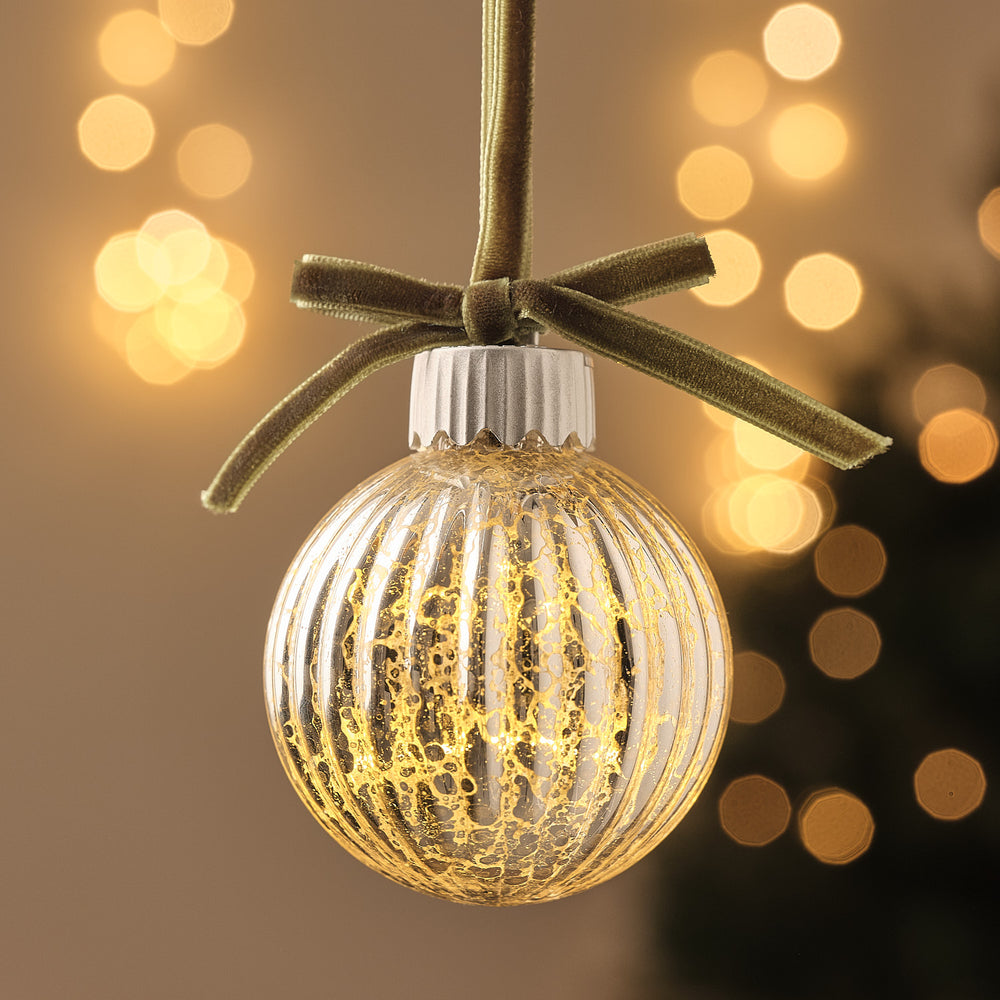 LED-Christbaumkugel aus Glas mit gerippter Oberfläche und grüner Schleife, warmweiß beleuchtet