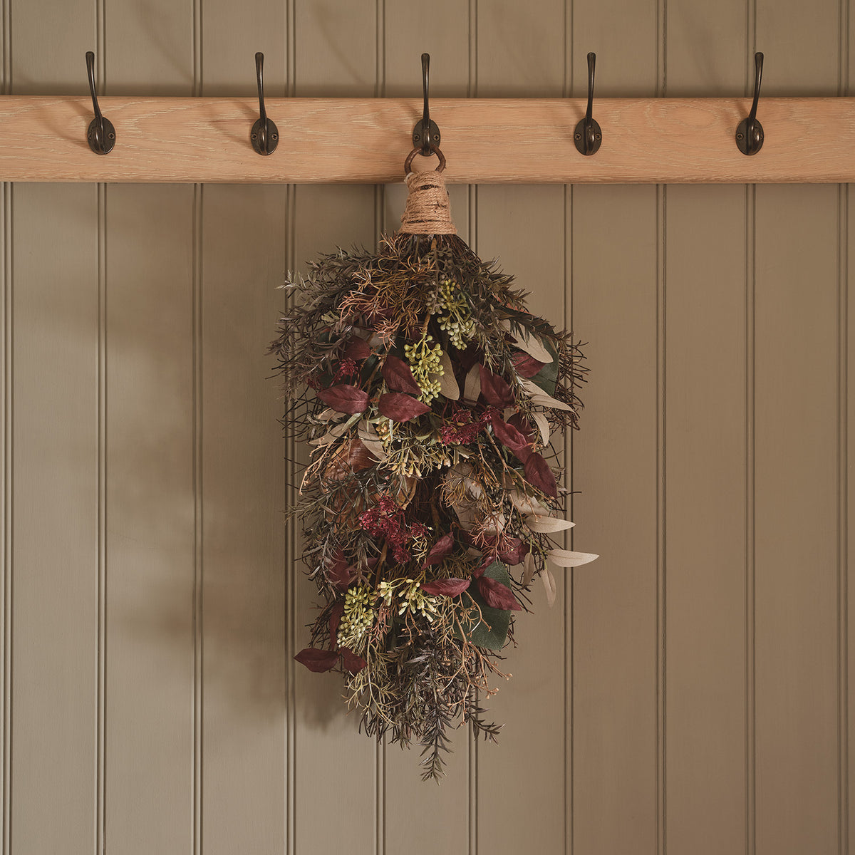 Herbstlicher Wandzweig mit künstlichen Blättern und Zweigen in Rot- und Grüntönen an einer weißen Tür