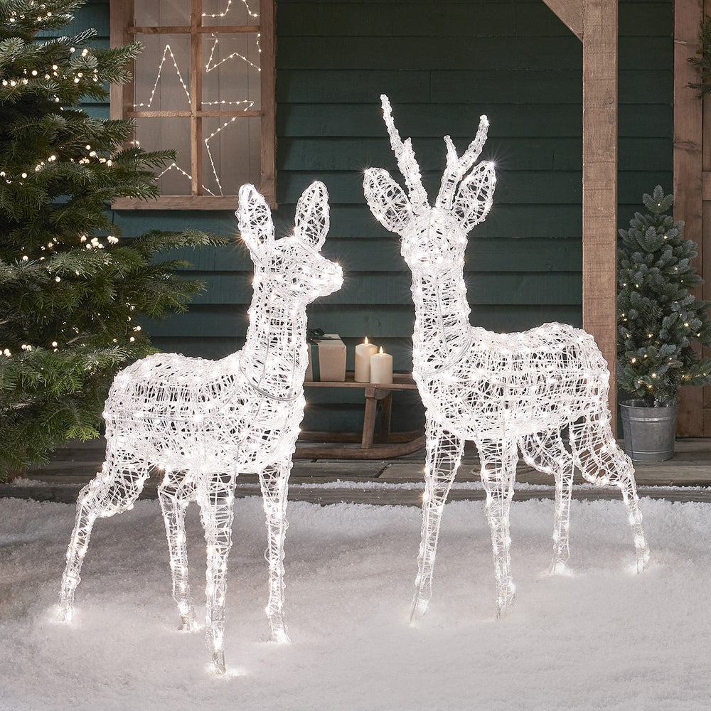 Zwei bicolore LED-Rentiere in weiß leuchtend vor Hauswand mit Weihnachtsdeko