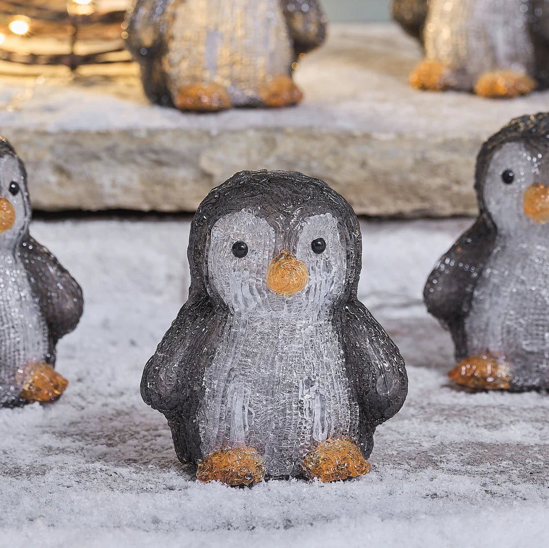 Detailaufnahme einer glitzernden Pinguin-Dekofigur mit strukturiertem grauem Schneeeffekt-Finish, goldenen Fußakzenten und aufgedruckten Augen, positioniert auf Stein-Oberfläche – hochwertige Winter-Dekofigur für gehobene Außen-Weihnachtsarrangements und dekorative Garten-Szenen.