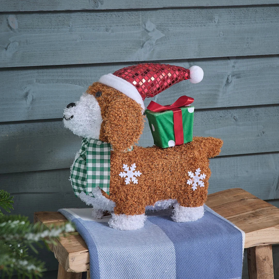 Beleuchtete braun-goldene Teddybär-Dekofigur mit warmweißer LED-Beleuchtung, roter gestrickter Weihnachtsmütze und kariertem grün-weißem Schal, positioniert auf blauem Holzblock mit weihnachtlichem Bokeh-Hintergrund – Premium-LED-Dekofigur für detailreiche Weihnachtsdisplays und gehobene festliche Raumdekorationen.