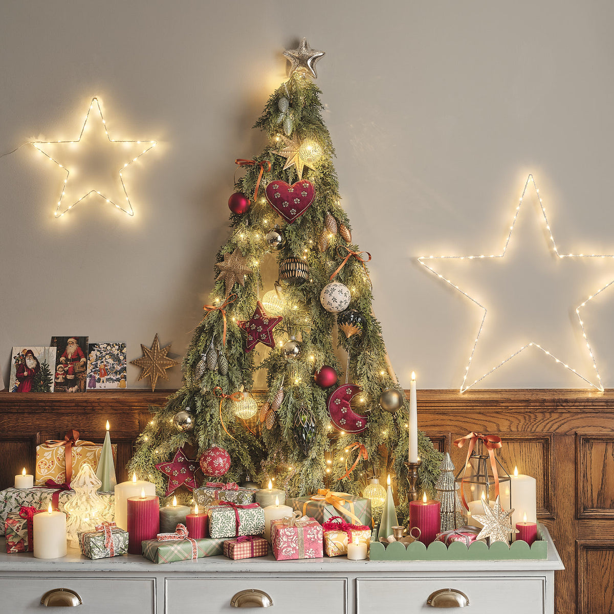 Detailansicht leuchtender Sterne am Weihnachtsbaum mit Geschenken darunter.