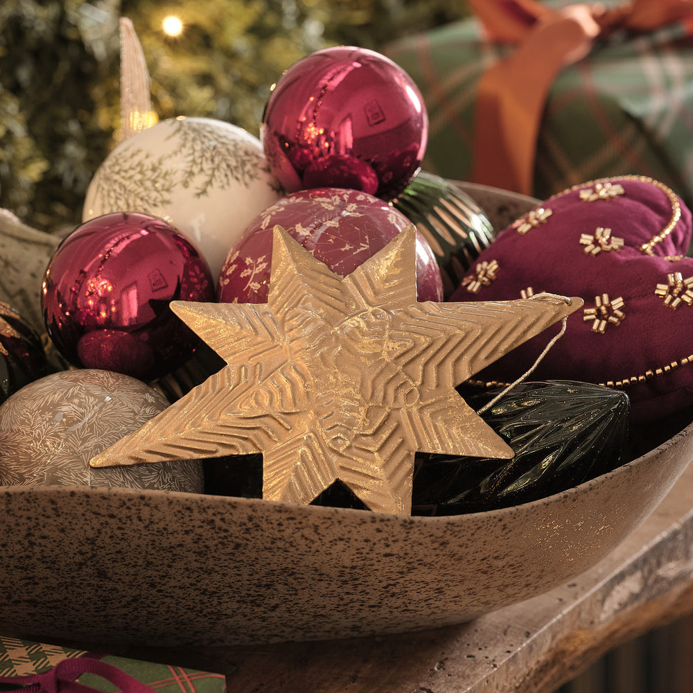 Holzschale mit bordeauxroten Weihnachtskugeln und goldenem Sternanhänger.