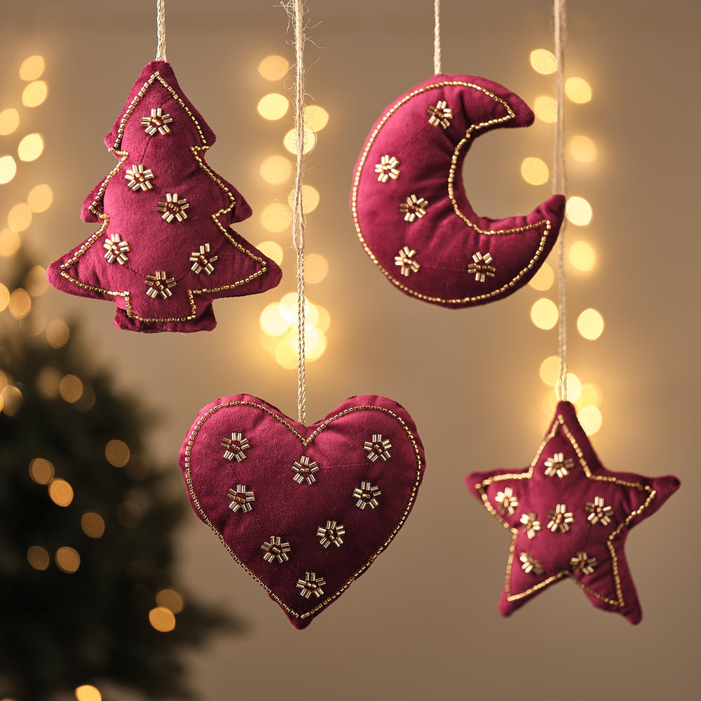 Bordeauxrote Stoff-Weihnachtsanhänger in Tannenbaum-, Mond-, Herz- und Sternform mit goldener Blumenstickerei, hängend vor Lichterglanz.