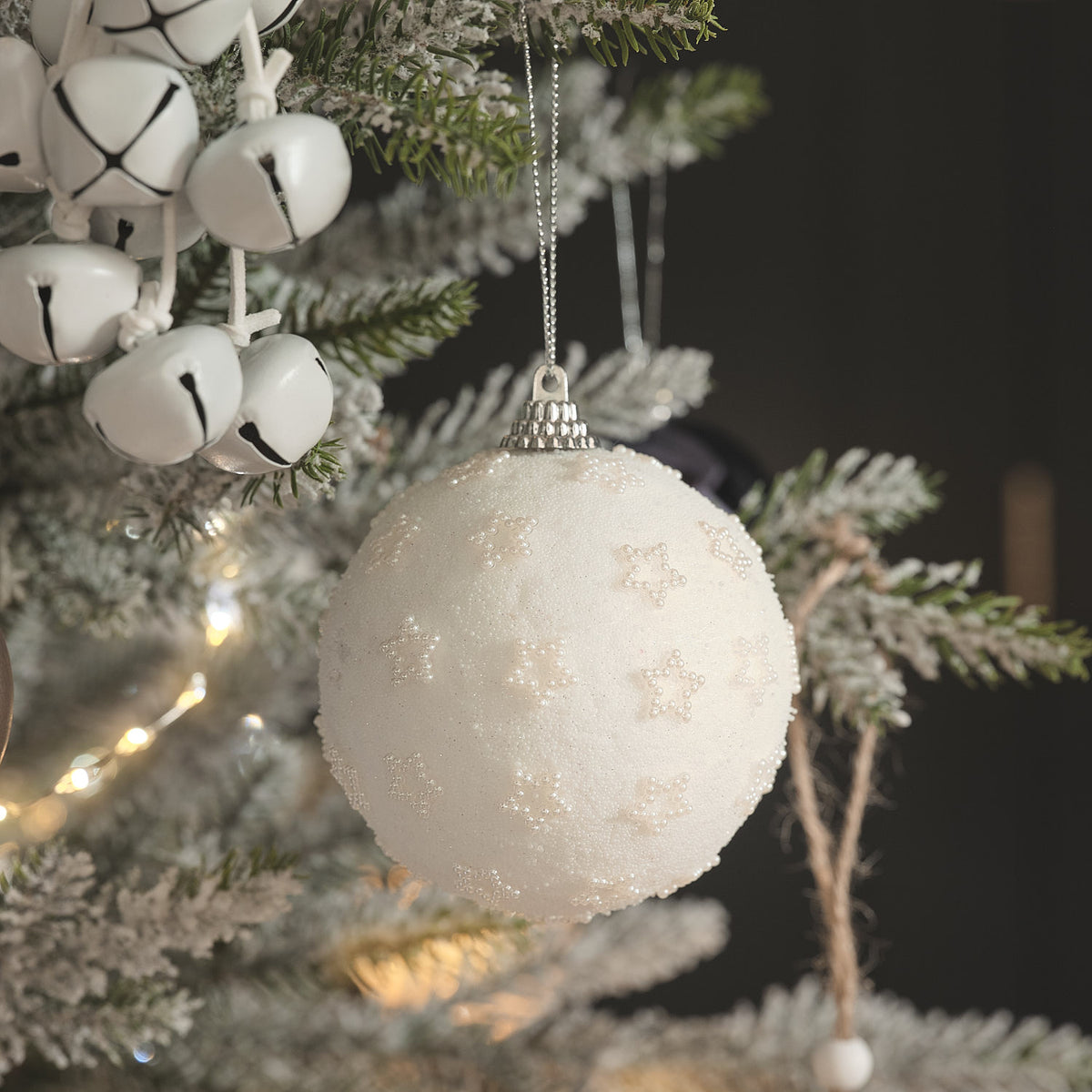 Weiße Weihnachtskugel mit Perlenbesatz an bereiftem Tannenzweig.