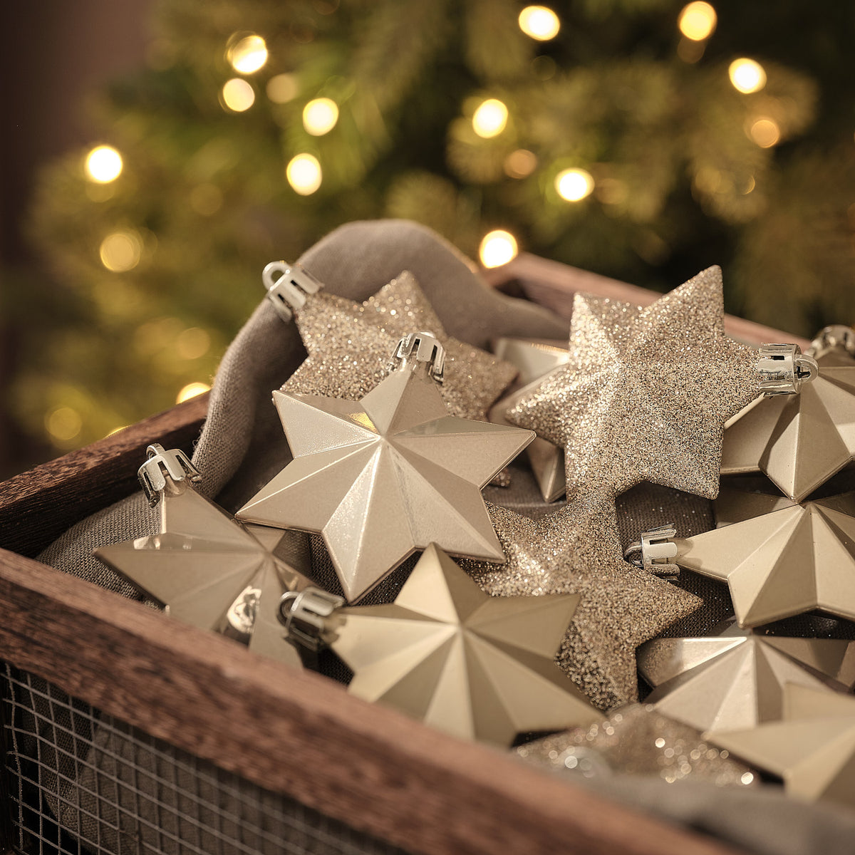 Goldene Sternförmige Weihnachtsanhänger mit Glitzer- und Facettenoptik in Holzkiste vor Lichterglanz.