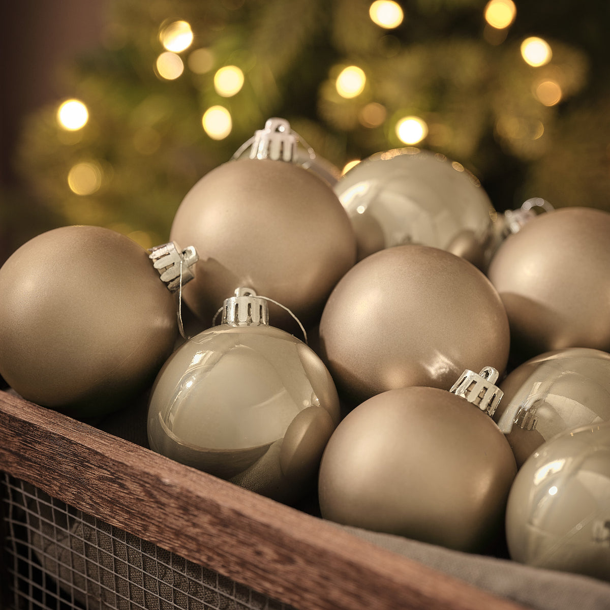 Bronzefarbene Weihnachtskugeln in matter und glänzender Optik in Holzkiste vor Lichterglanz.