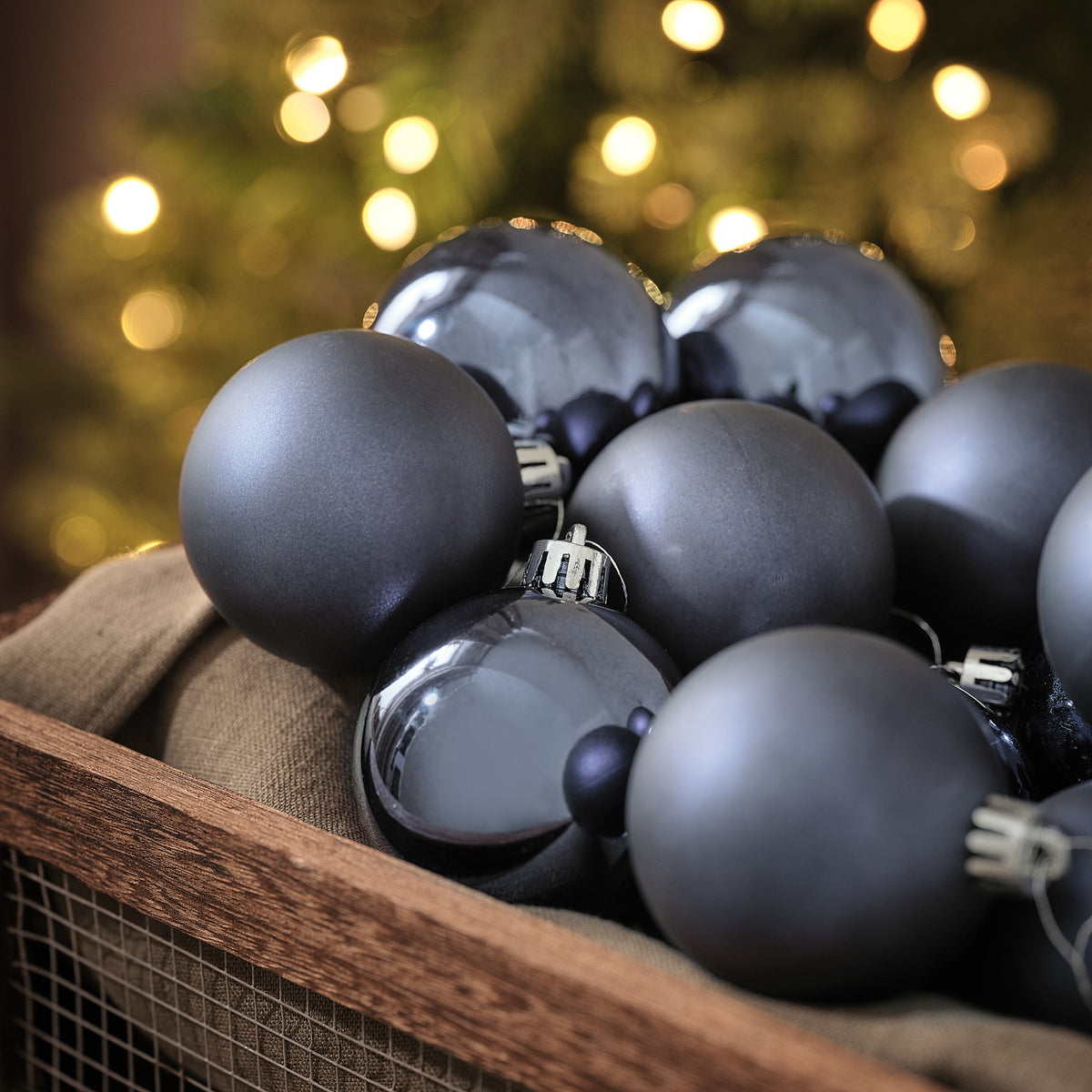 Blaue Weihnachtskugeln in matter und glänzender Optik in Holzkiste vor Lichterglanz.