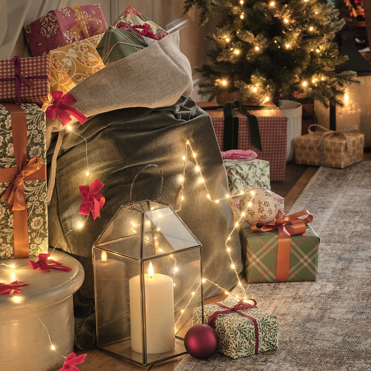 Metall-Laterne mit Kerze neben Geschenken und Weihnachtsbaum.