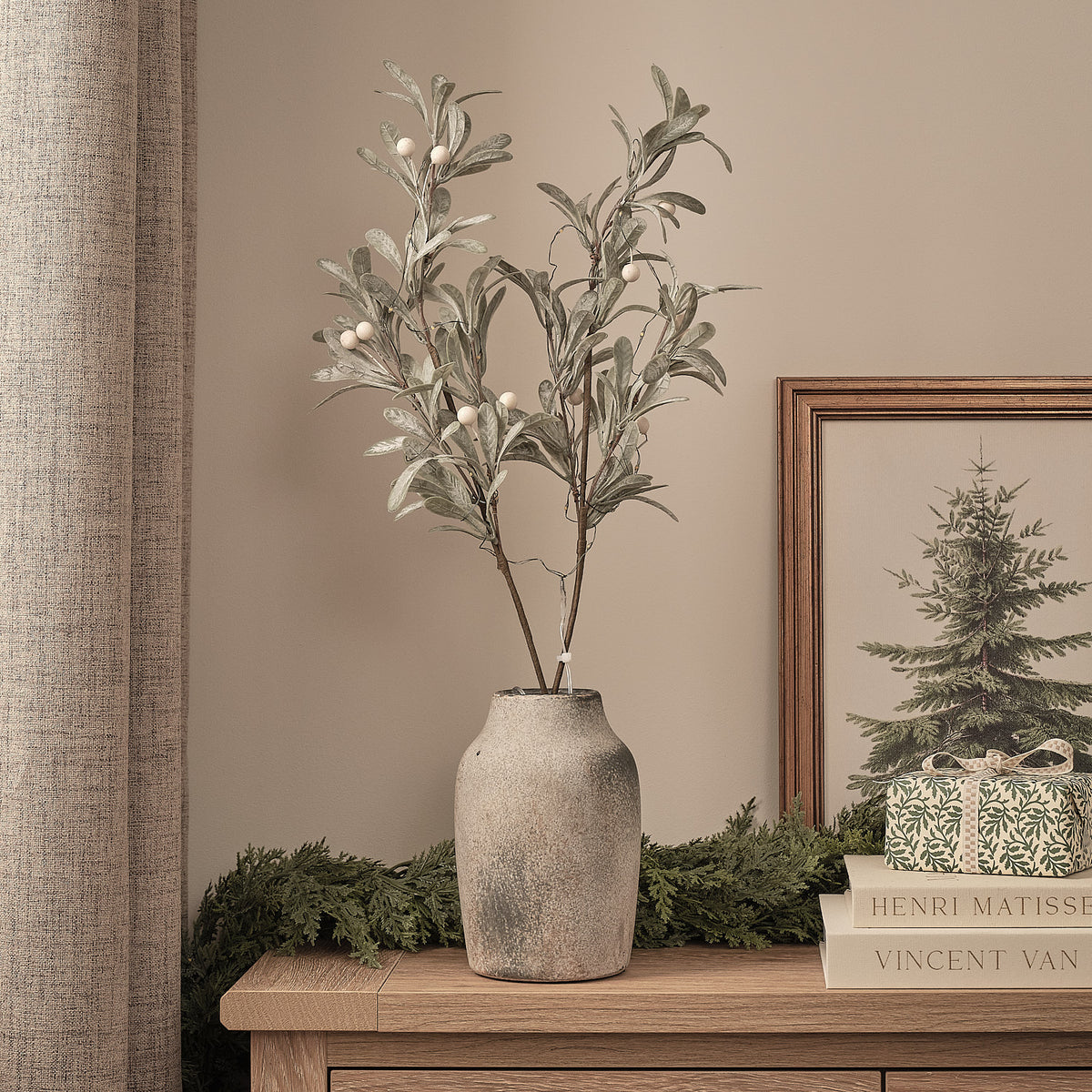 Künstliche Mistelzweige ohne Beleuchtung in grauer Vase neben Weihnachtsbild und Geschenk