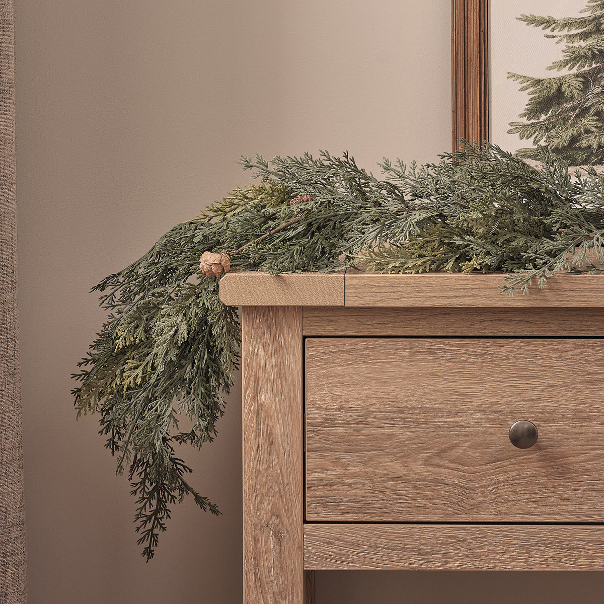 Detailansicht beleuchtete Weihnachtsgirlande mit Tannenzapfen auf Holzkommode vor neutraler Wand